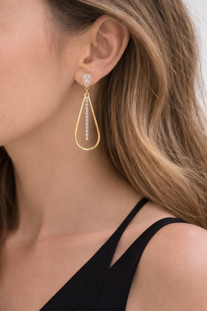 Gold teardrop earrings with clear gemstones worn by a person with shoulder-length hair.